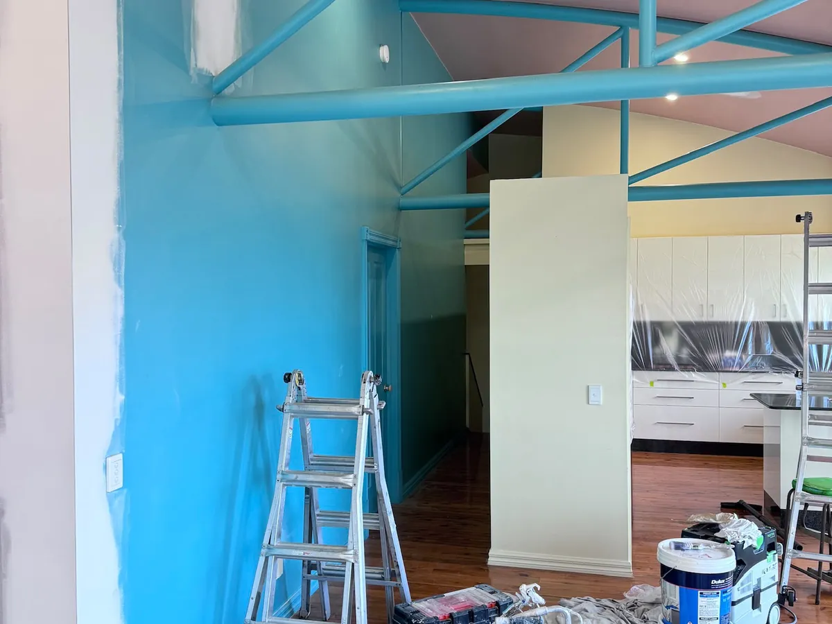 Commercial fit-out mid-repaint with exposed teal structural beams and recessed lighting