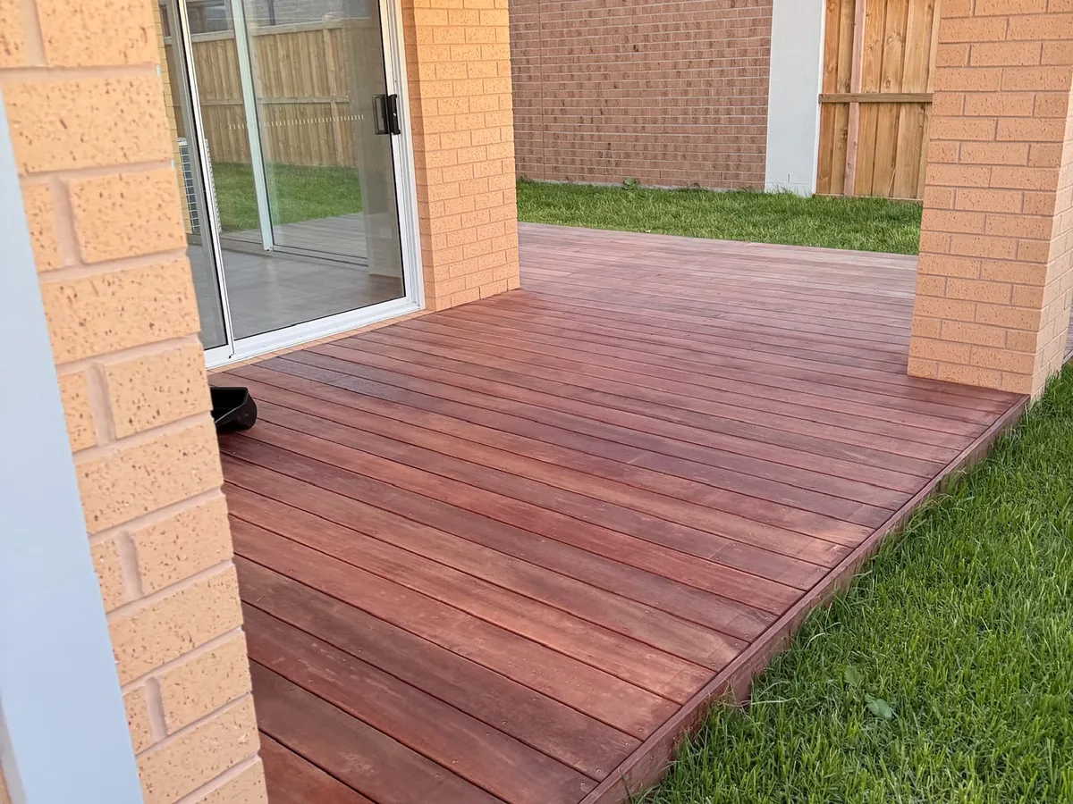 Freshly stained timber deck running alongside a brick home with glass sliding doors