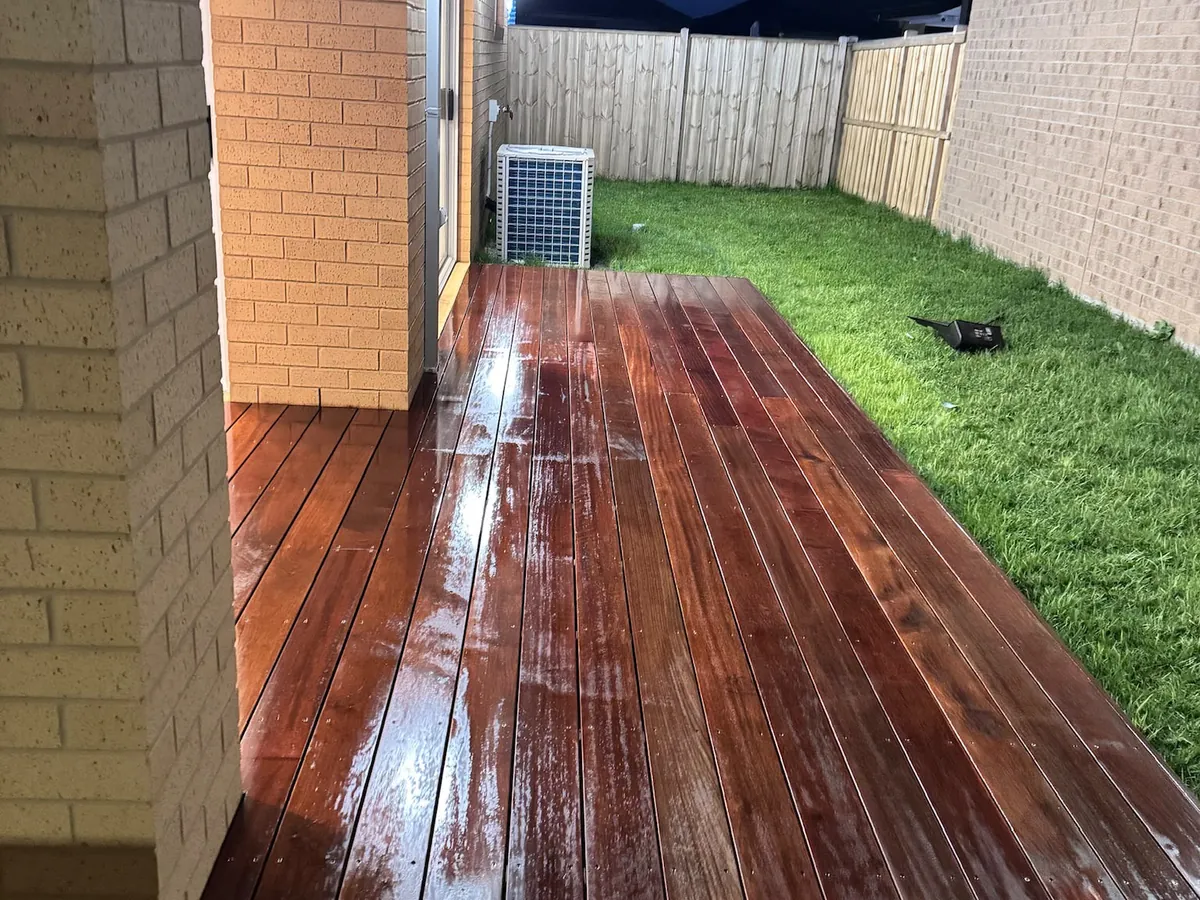 Glossy freshly coated timber deck reflecting the brick home behind it